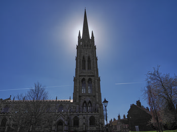 St James Spire Spring 2 This architectural photograph captures St James' Spire, the prominent tower of St James' Church in Louth, Lincolnshire, positioned against a bright midday sky. It is springtime, as evidenced by the budding trees and clear conditions, which complement the church's stone façade. The urban setting is highlighted by surrounding historic buildings, typical of Louth, and there is a noticeable contrail in the sky, adding a dynamic element to the composition. The image was taken in the afternoon, showcasing the church as a significant landmark and example of urban architecture in Lincolnshire during the spring season.